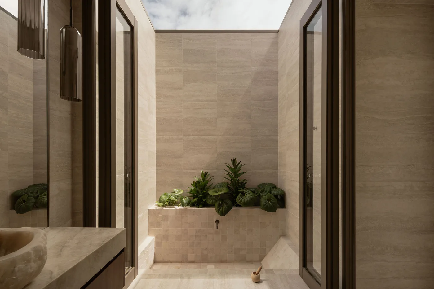 A skylit internal courtyard at ZOEI with travertine walls and layered planting.