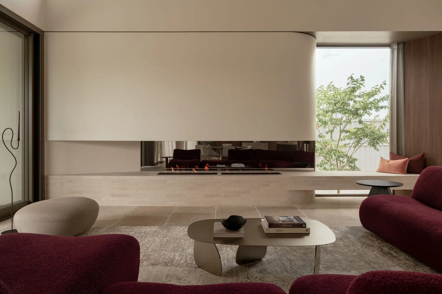 The living room at ZOEI, a luxury photoshoot location on the Gold Coast, with a sculptural fireplace, limestone floors and deep wine bouclé seating.