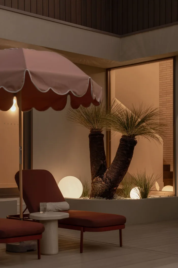 A scalloped umbrella and planting lit at dusk in the ZOEI courtyard.